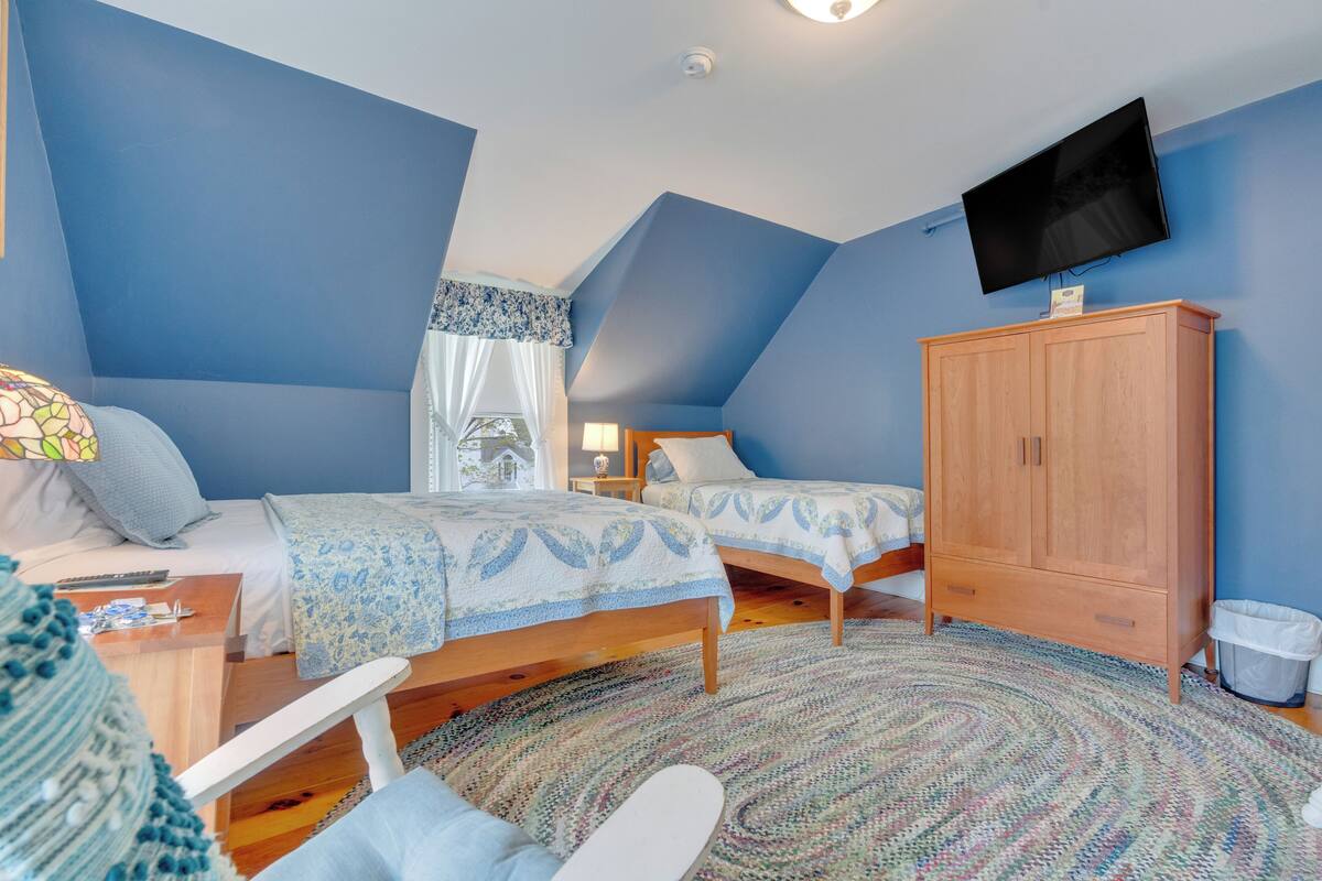 A bedroom with two beds, a TV, a wooden cabinet, and a patterned rug.