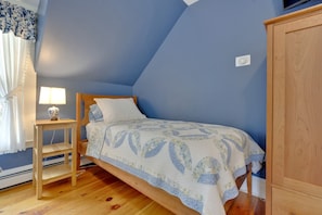 A bedroom with a single bed, a bedside table with a lamp, a wooden wardrobe, and a window with curtains.