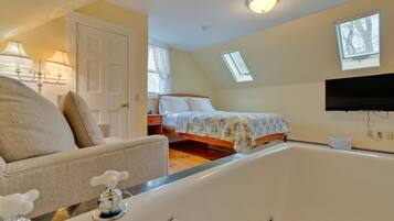 A bedroom with a large bathtub, a bed with floral bedding, a TV mounted on the wall, and a skylight.