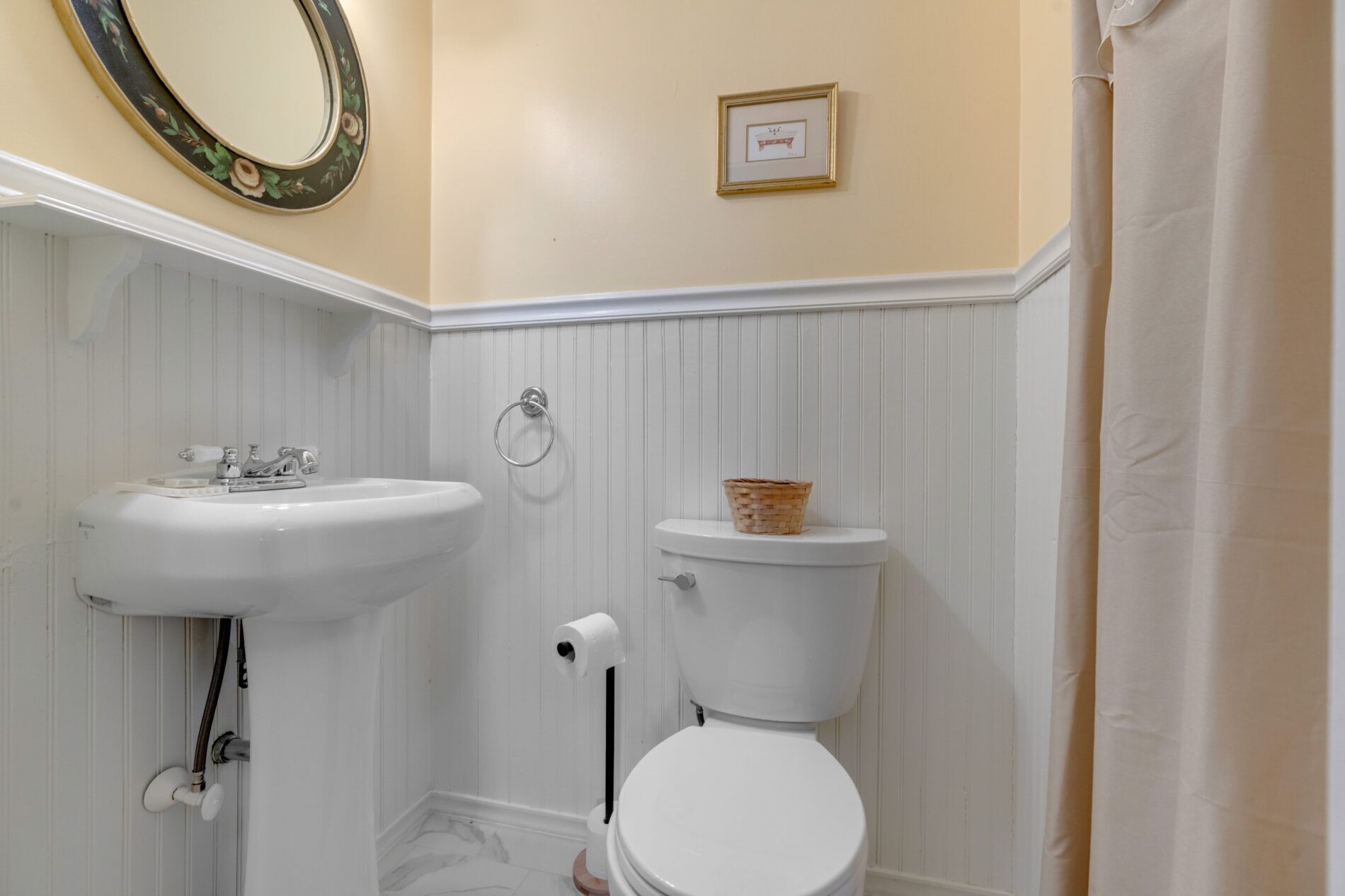 A bathroom with a white sink, toilet, and a mirror with a floral frame.