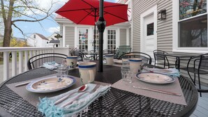 An outdoor dining area with a red umbrella, metal chairs, and a table set for two.