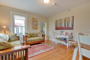 A living room with a sofa, chairs, a coffee table, a rug, and a bookshelf with books and magazines.