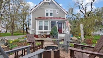 A house with a front porch, a fire pit, and two Adirondack chairs.