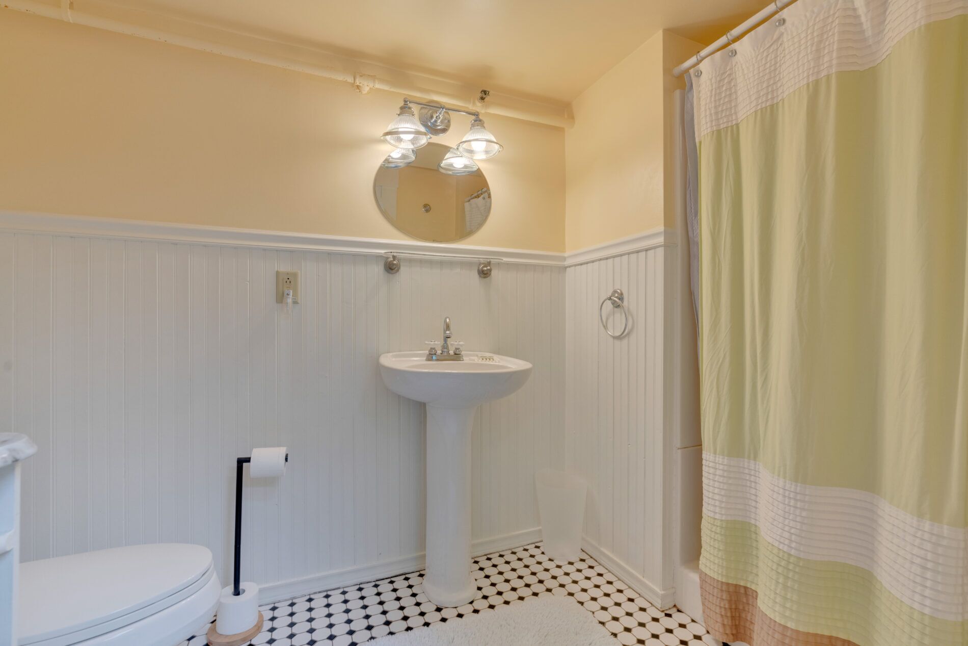 A bathroom with a white pedestal sink, a toilet, a mirror above the sink, and a shower curtain.