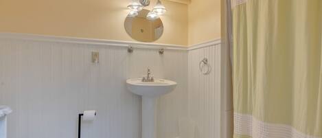 A bathroom with a white pedestal sink, a toilet, a mirror above the sink, and a shower curtain.