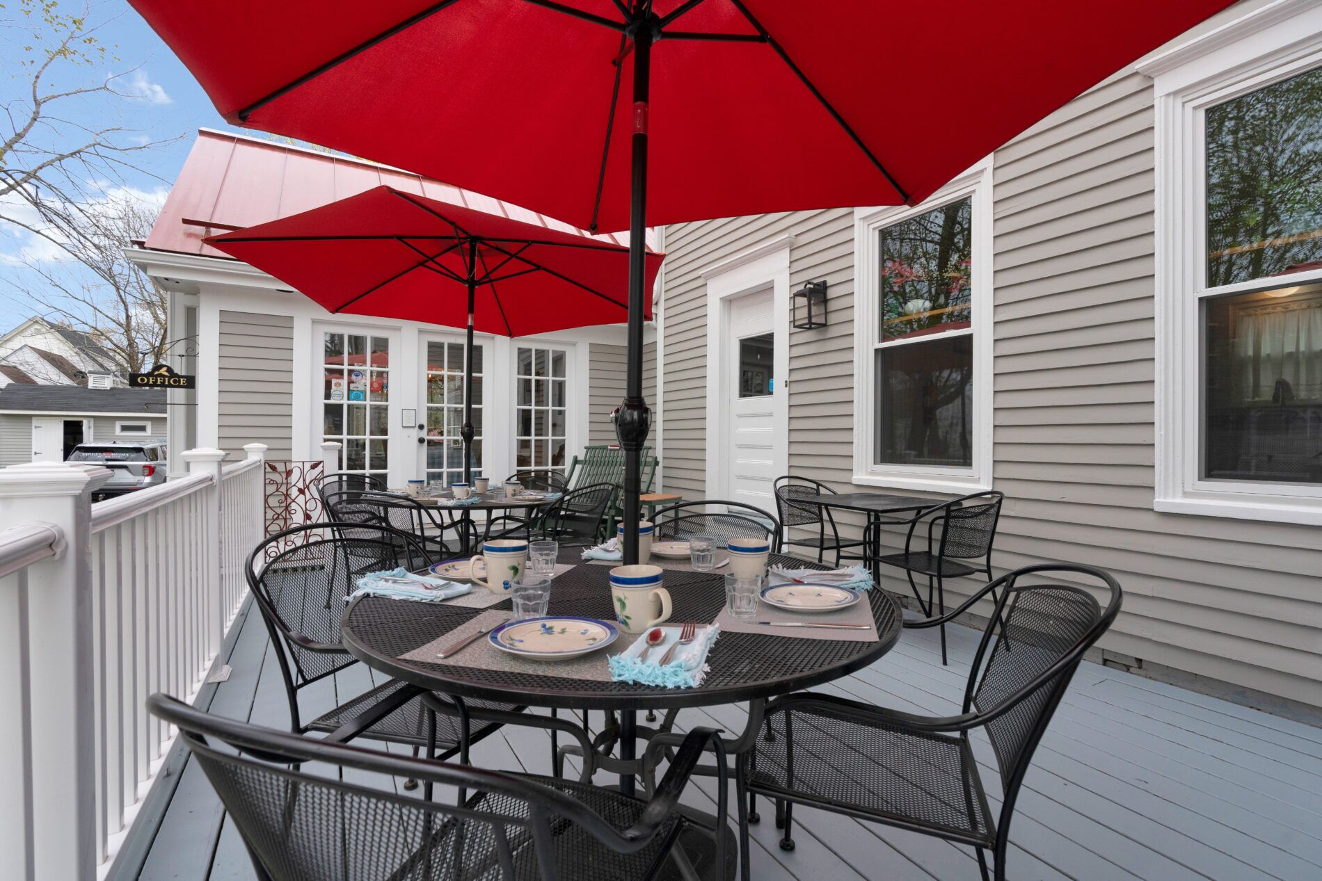 An outdoor patio with a round table, chairs, and a red umbrella.
