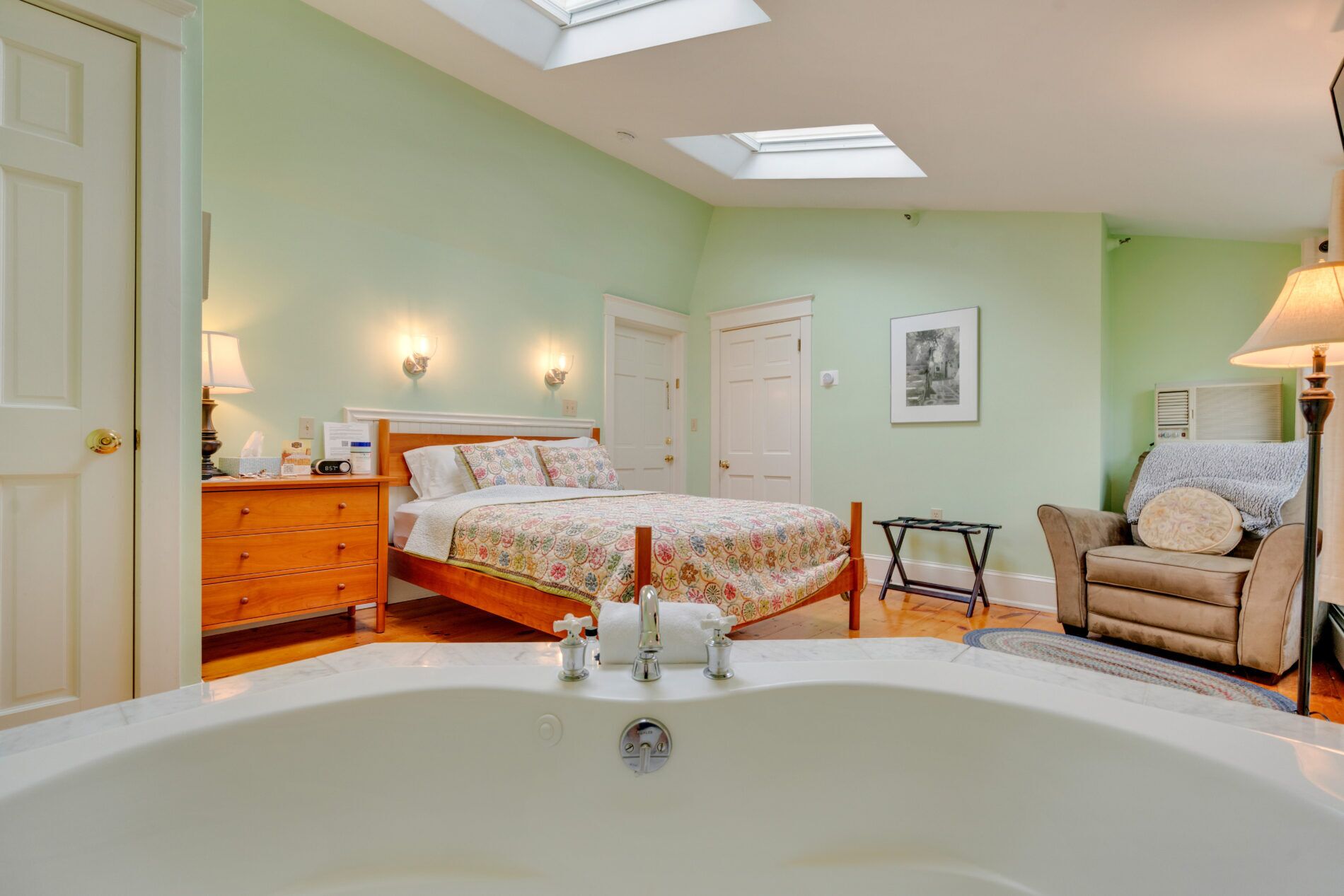 Une chambre à coucher avec une grande baignoire, un lit avec une literie à motifs floraux, une chaise et un bureau avec une lampe.