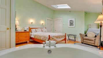 Une chambre à coucher avec une grande baignoire, un lit avec une literie à motifs floraux, une chaise et un bureau avec une lampe.