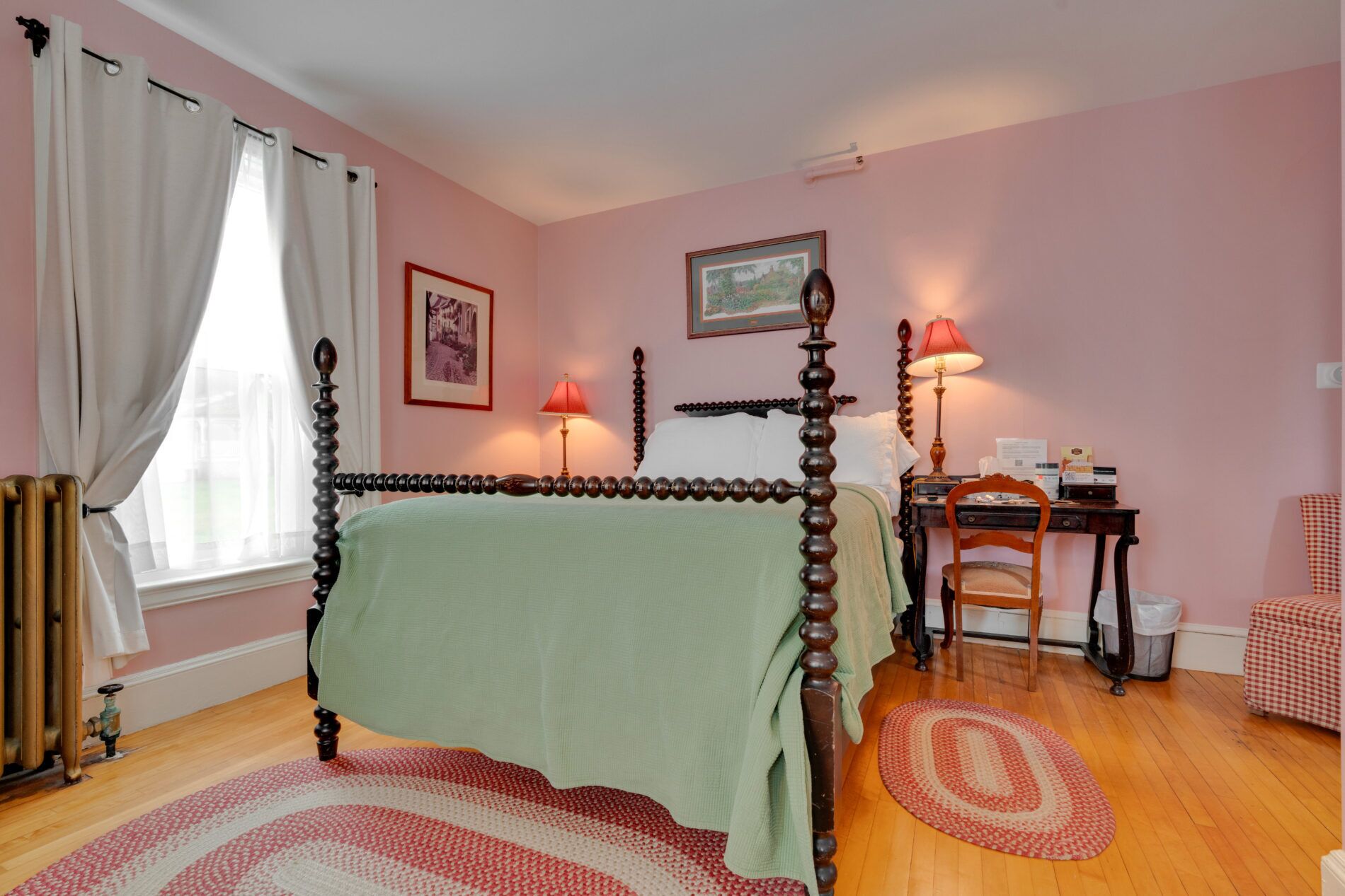 Un dormitorio con cama con dosel, un escritorio con silla, un radiador y una ventana con cortinas.