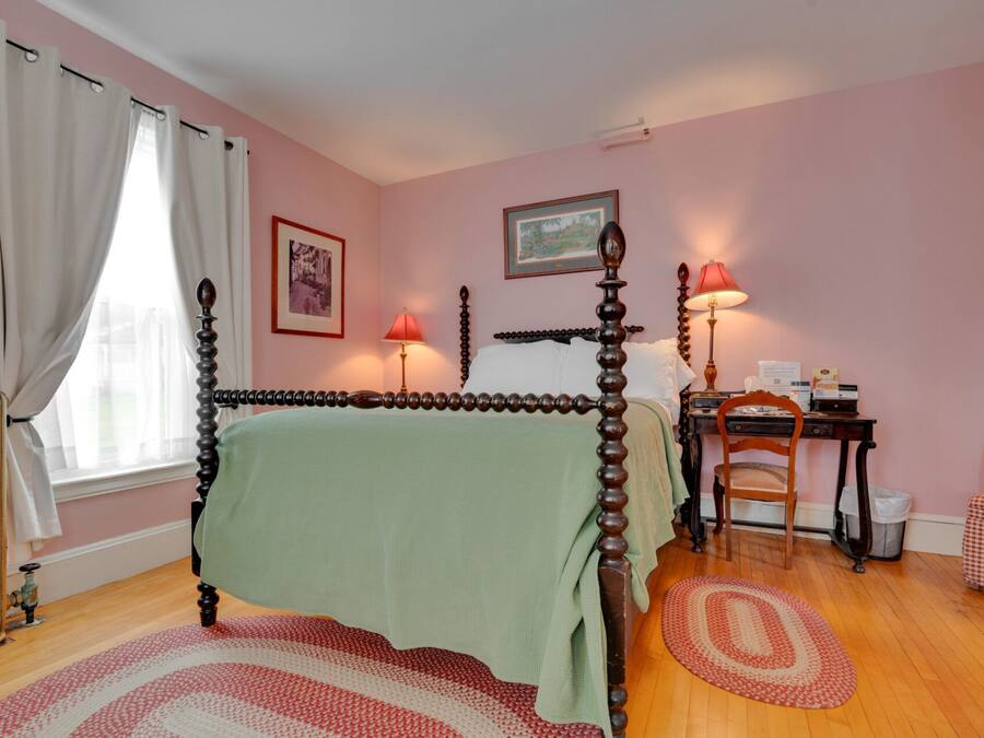 Un dormitorio con cama con dosel, un escritorio con silla, un radiador y una ventana con cortinas.