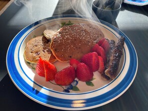 Un plato con tortitas, fresas y salchichas.
