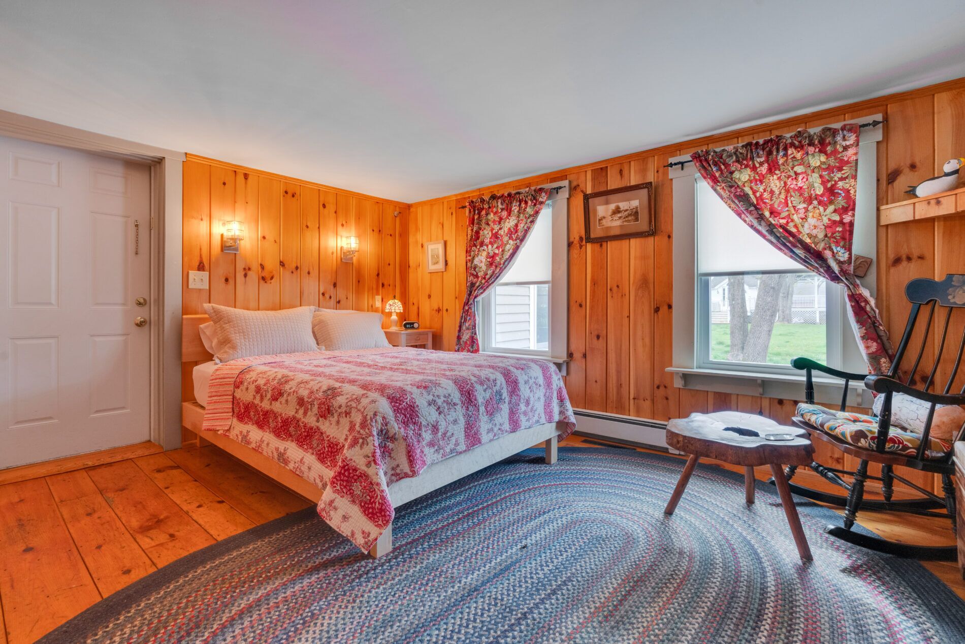 Ein Schlafzimmer mit einem Bett, einem Sessel, einem kleinen Tisch und einem Fenster mit Vorhängen.