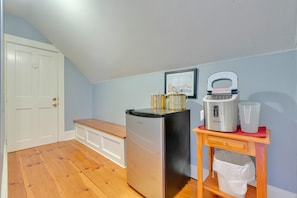A compact kitchen with a refrigerator, a coffee maker, and a trash bin on a wooden table.