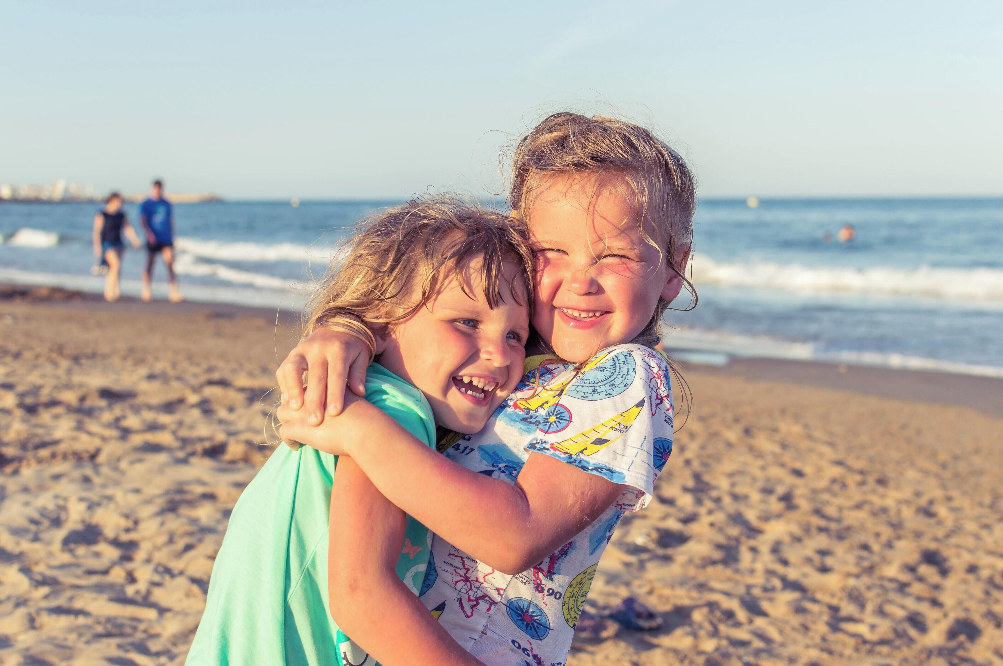 Dos niños abrazándose en la playa, con olas al fondo.