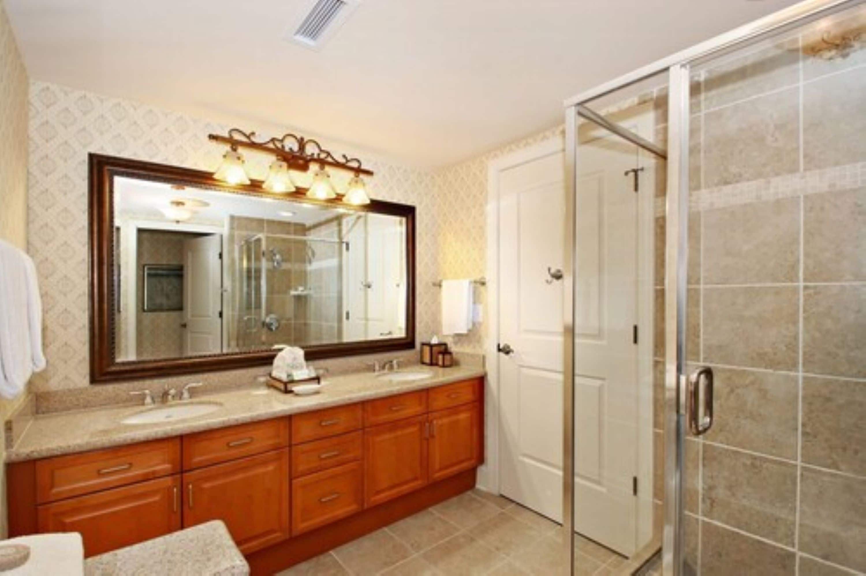 A bathroom with a large mirror, a sink, a vanity, and a shower area.