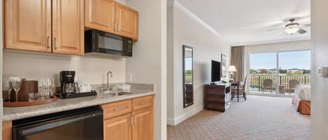 A modern kitchen with wooden cabinets, a microwave, and a dishwasher. There is a dining area with a table and chairs, and a balcony with a view.