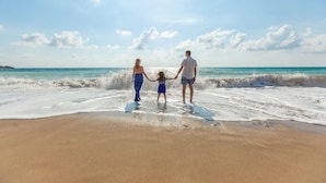 A family holding hands on a sandy beach with waves, under a clear sky.