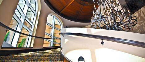 A spiral staircase with patterned carpet, a wooden ceiling, and a wrought iron railing.