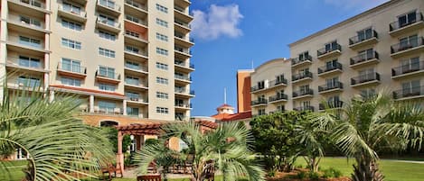 Un hotel de varios pisos con balcones, un patio con palmeras y un edificio con techo rojo.
