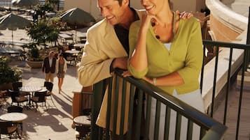 Una pareja en un balcón con vista a un puerto deportivo con barcos, asientos al aire libre y vistas al agua.