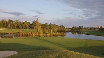 Un campo de golf con un estanque, árboles y cielo despejado.