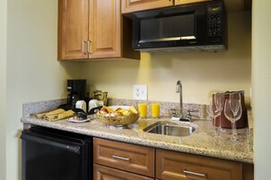 Una cocina con armarios de madera, microondas, cafetera, pileta y un bol con fruta.