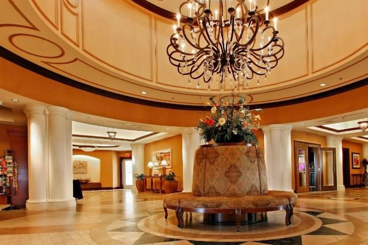 A spacious lobby with a central seating area, a chandelier, and a reception desk.
