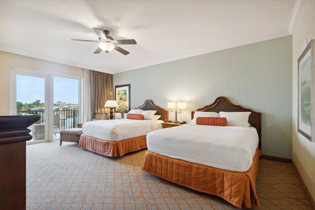 A hotel room with two beds, a ceiling fan, a balcony with a view, and a pool table.