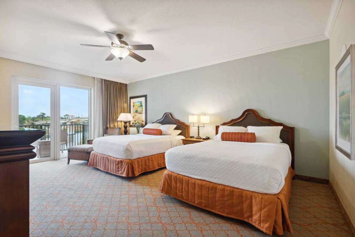A hotel room with two beds, a ceiling fan, a balcony, and a view of the outside.
