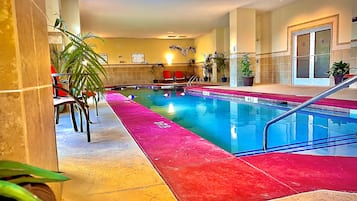 An indoor swimming pool with a red and yellow tiled floor, surrounded by chairs and potted plants.