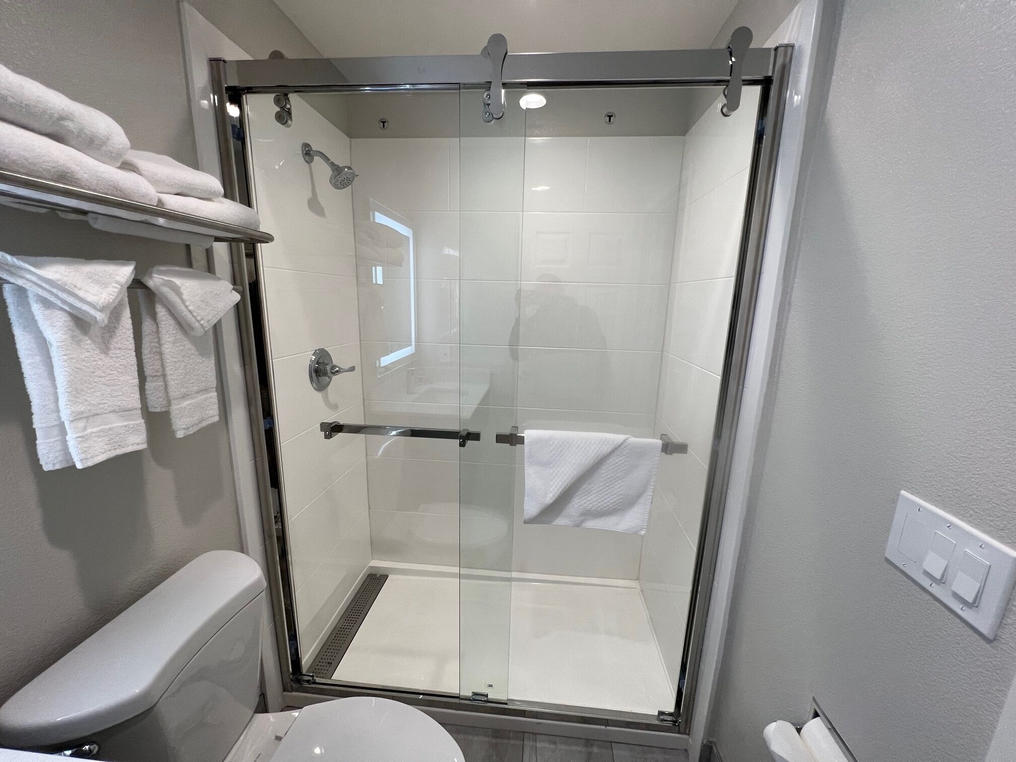 A modern bathroom with a glass-enclosed shower, a toilet, and a towel rack with folded towels.