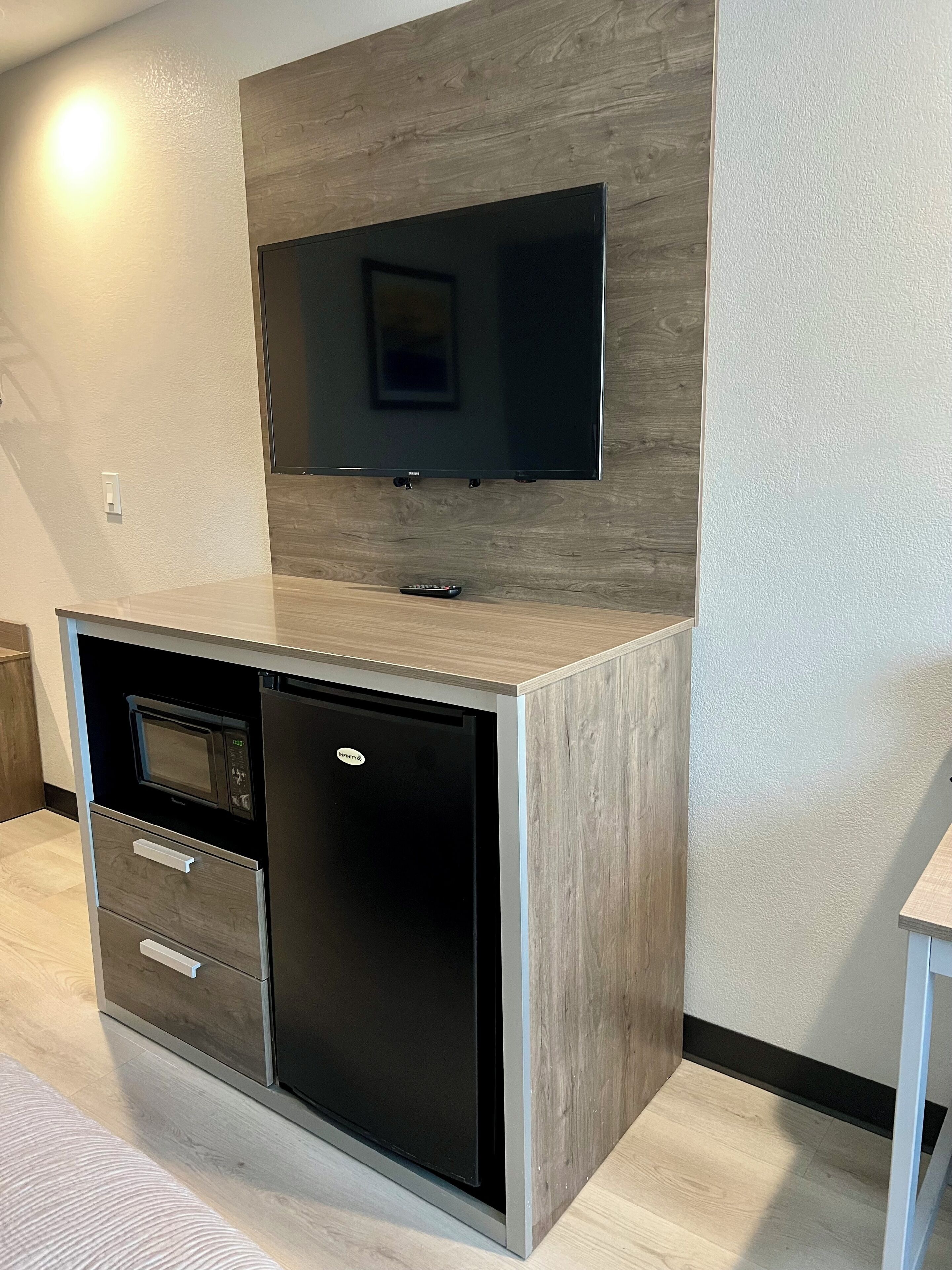 A modern kitchen with a built-in microwave, a refrigerator, and a flat-screen TV mounted on a wooden wall.