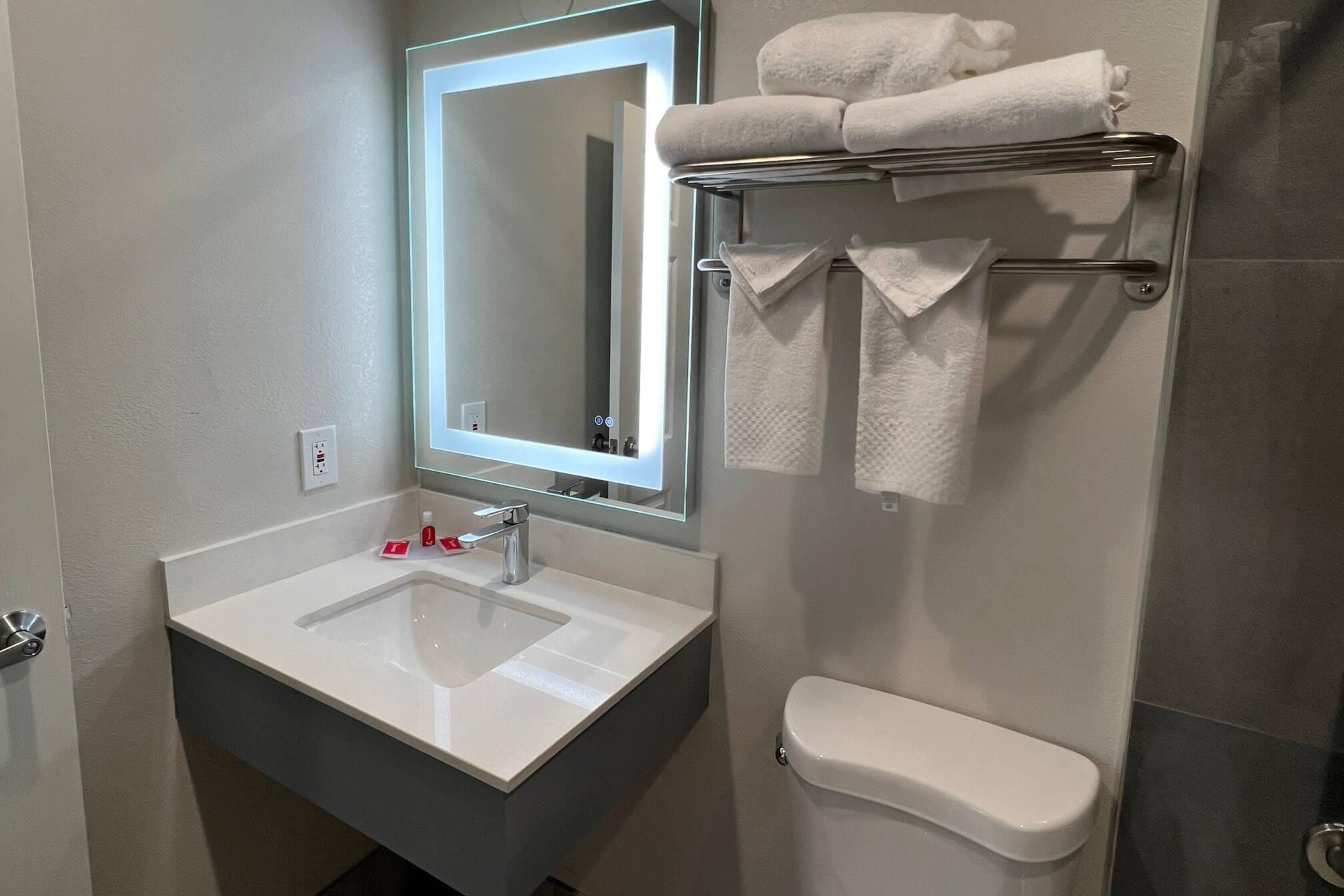 A bathroom with a white sink, a mirror, a toilet, and a towel rack with towels.