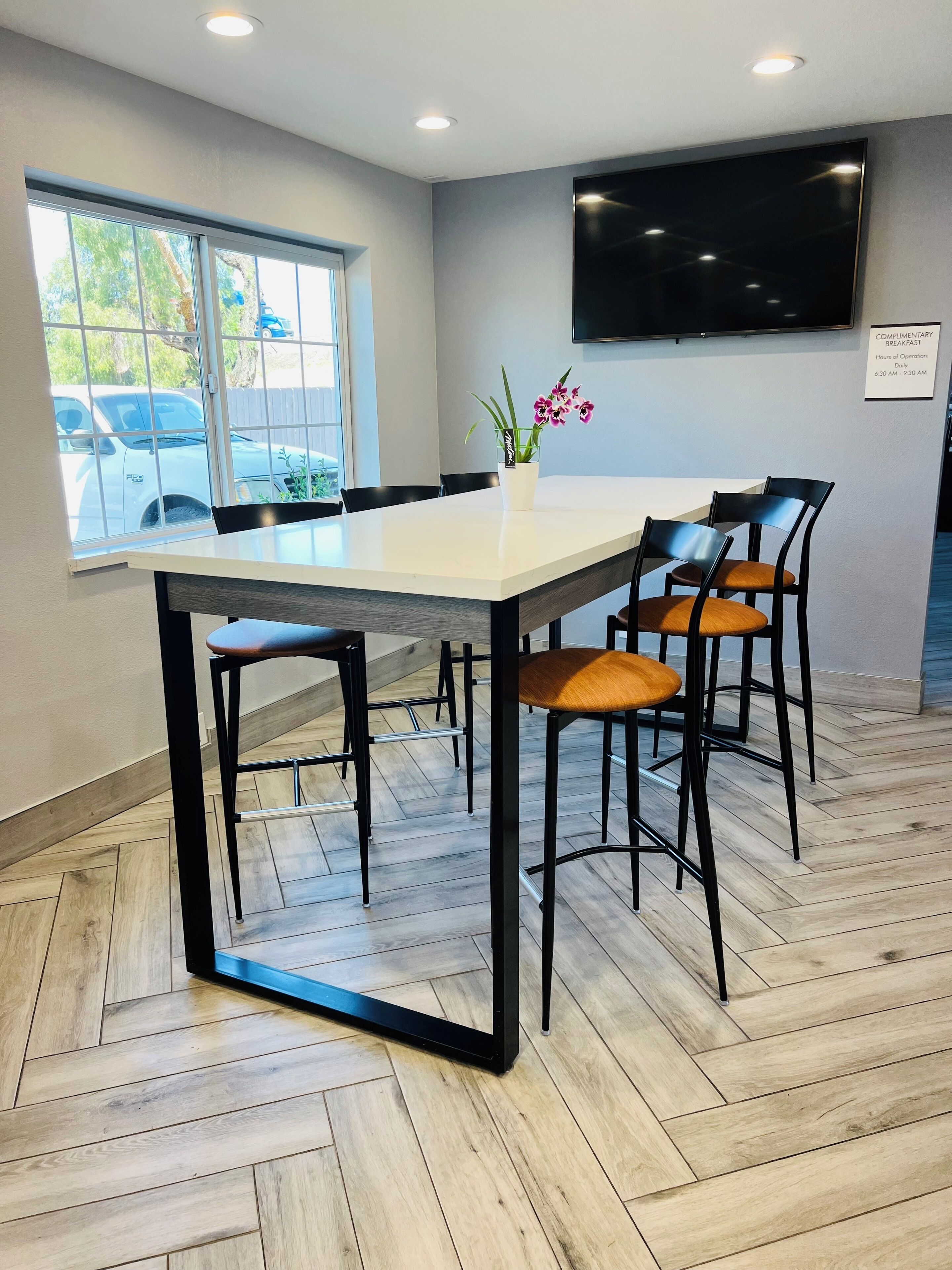 A conference room with a large table, four chairs, a potted plant, and a sign indicating complimentary breakfast hours.