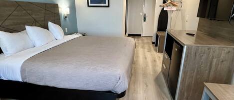 A hotel room with a large bed, a desk, a kitchenette, and a bathroom.