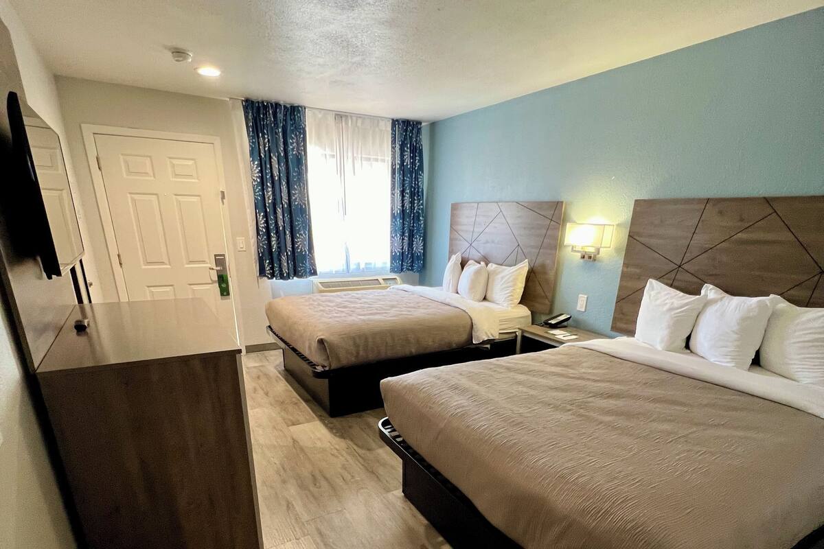 A hotel room with two beds, a TV, a desk, and a window with curtains.