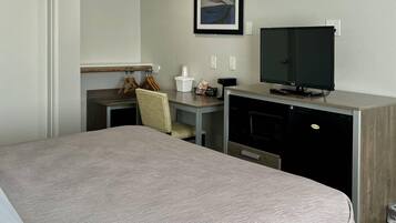 A hotel room with a bed, a desk with a television, a chair, and a small kitchenette area.