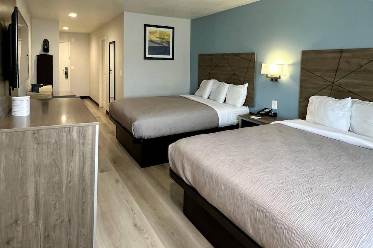 Une chambre d’hôtel avec deux lits, un bureau, une télévision et un tableau au mur.