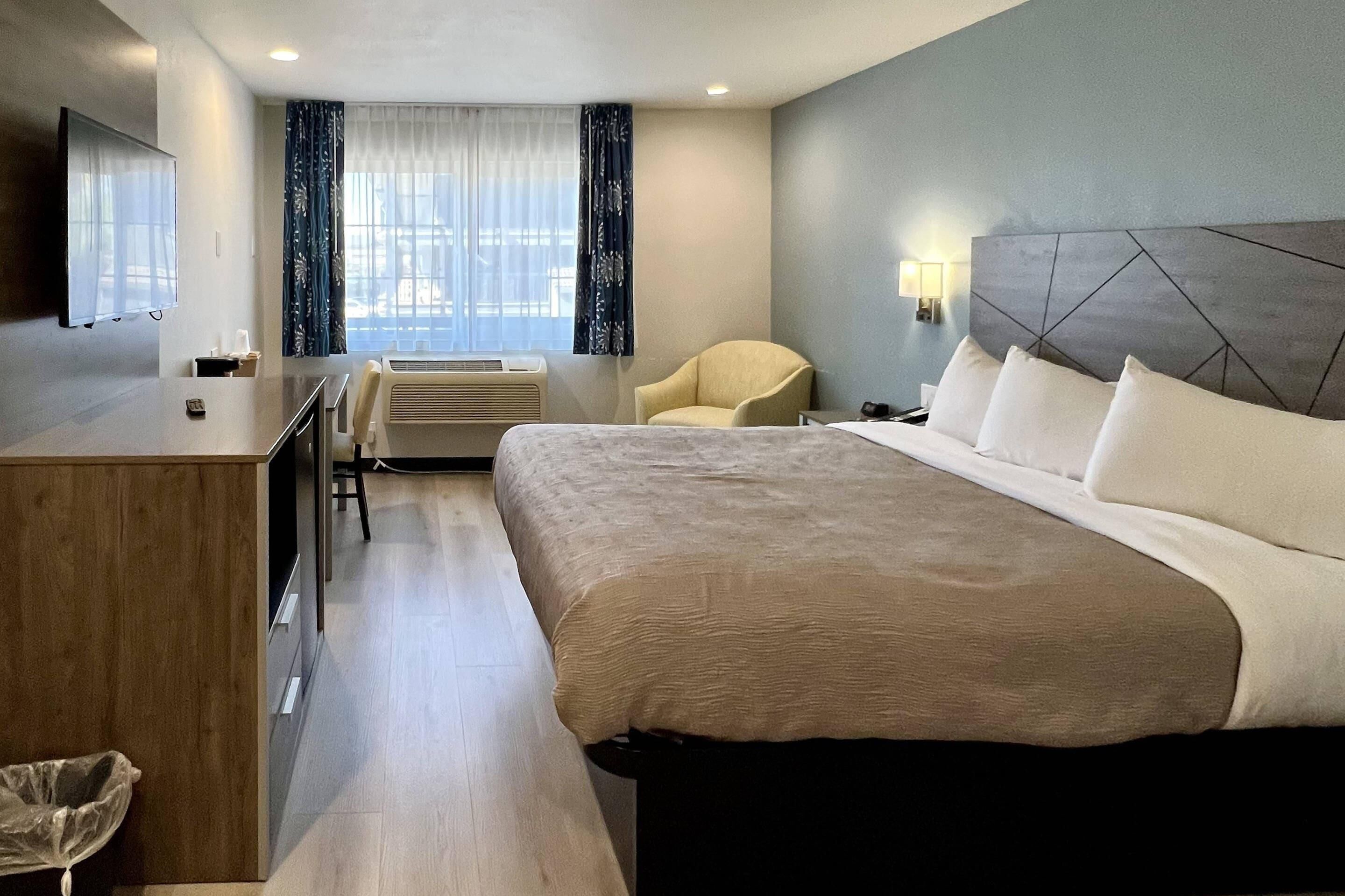 A hotel room with a bed, a desk, a chair, a TV, and a window with curtains.