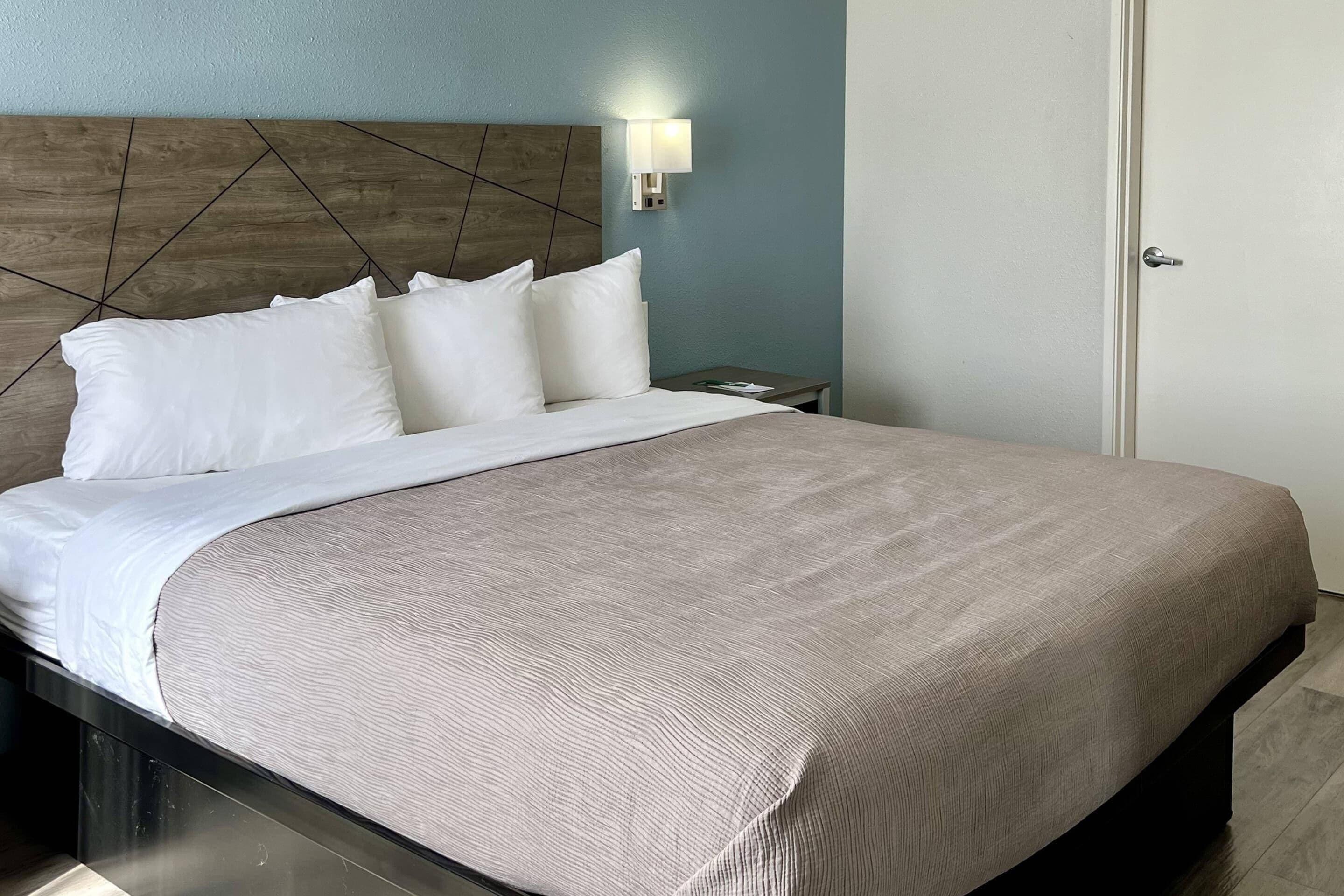 A neatly made bed with a headboard, a bedside table, a wall-mounted light, and a door.