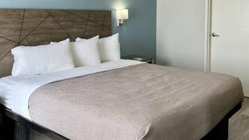 A neatly made bed with a headboard, a bedside table, a wall-mounted light, and a door.