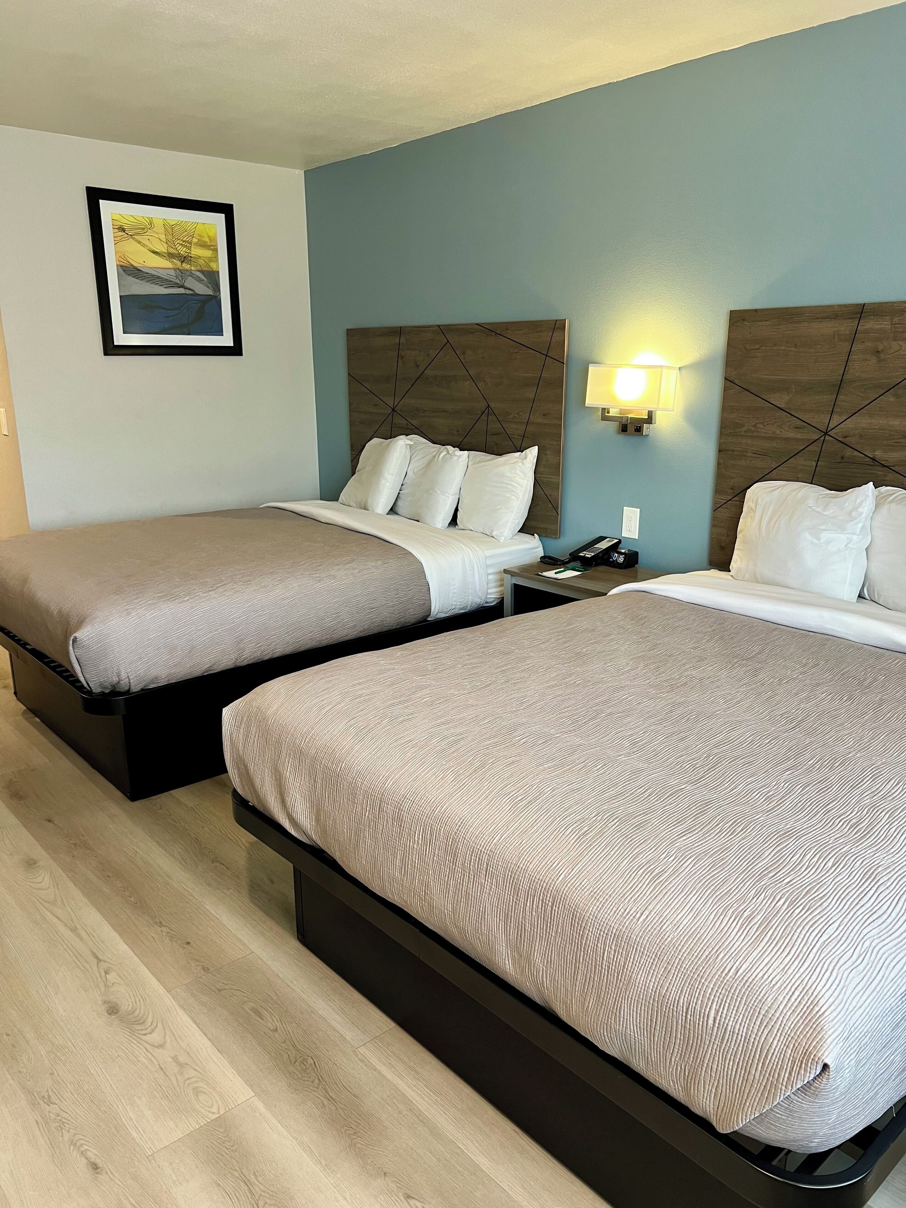 A hotel room with two beds, a nightstand, a lamp, and a framed picture on the wall.
