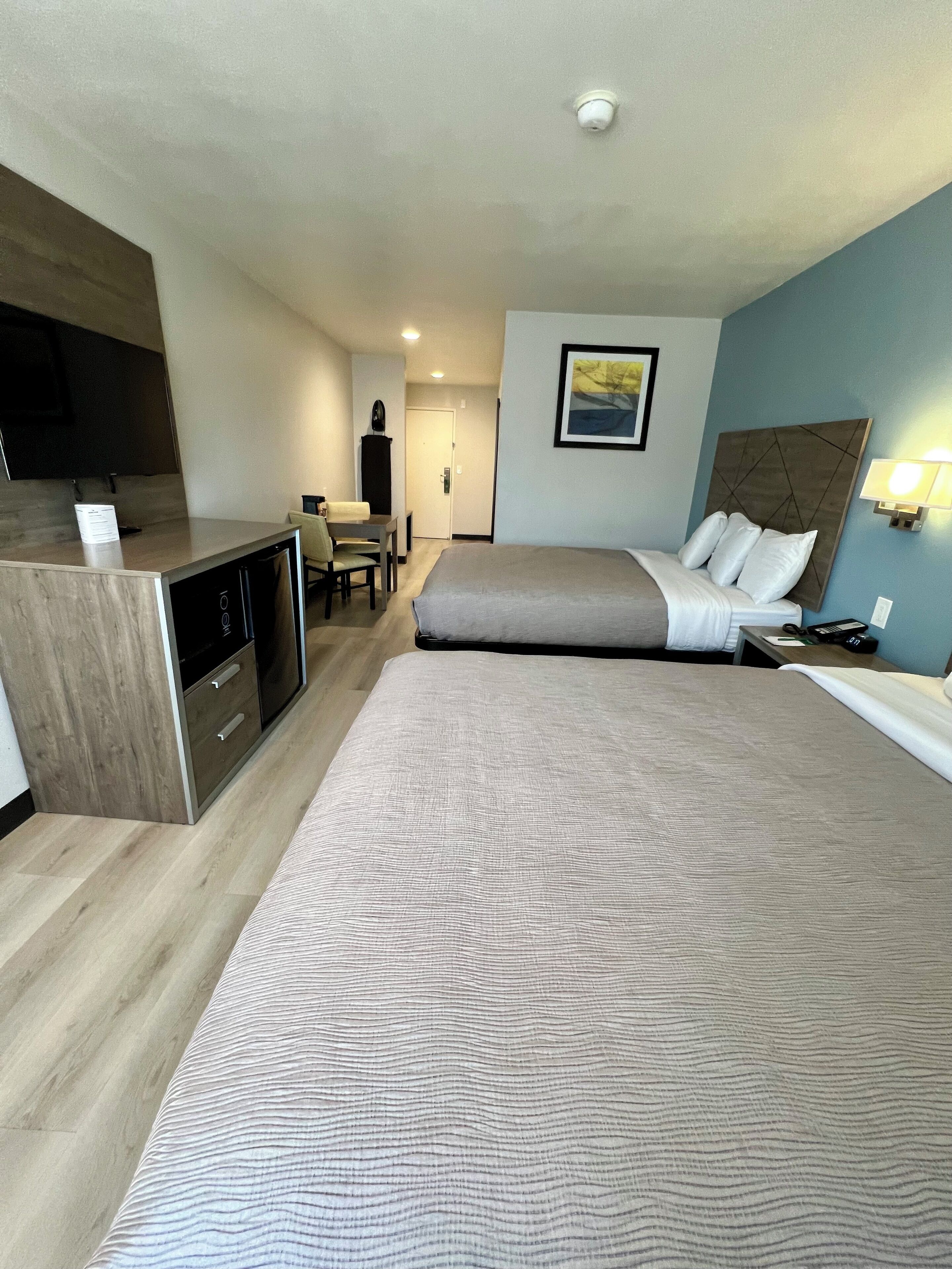 A hotel room with a bed, a desk, a chair, a TV, and a painting on the wall.