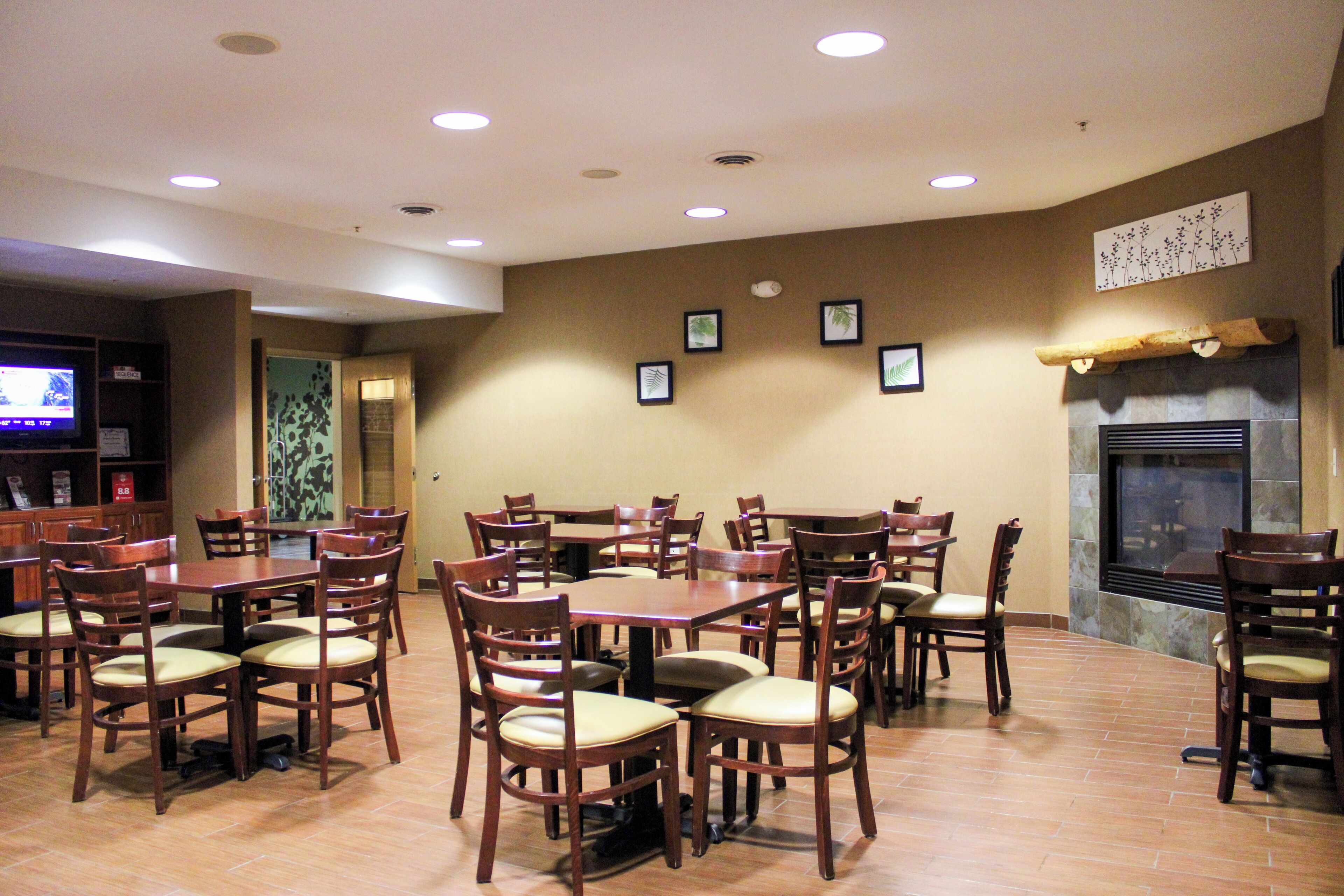 A dining area with multiple wooden tables and chairs, a television, and a fireplace.
