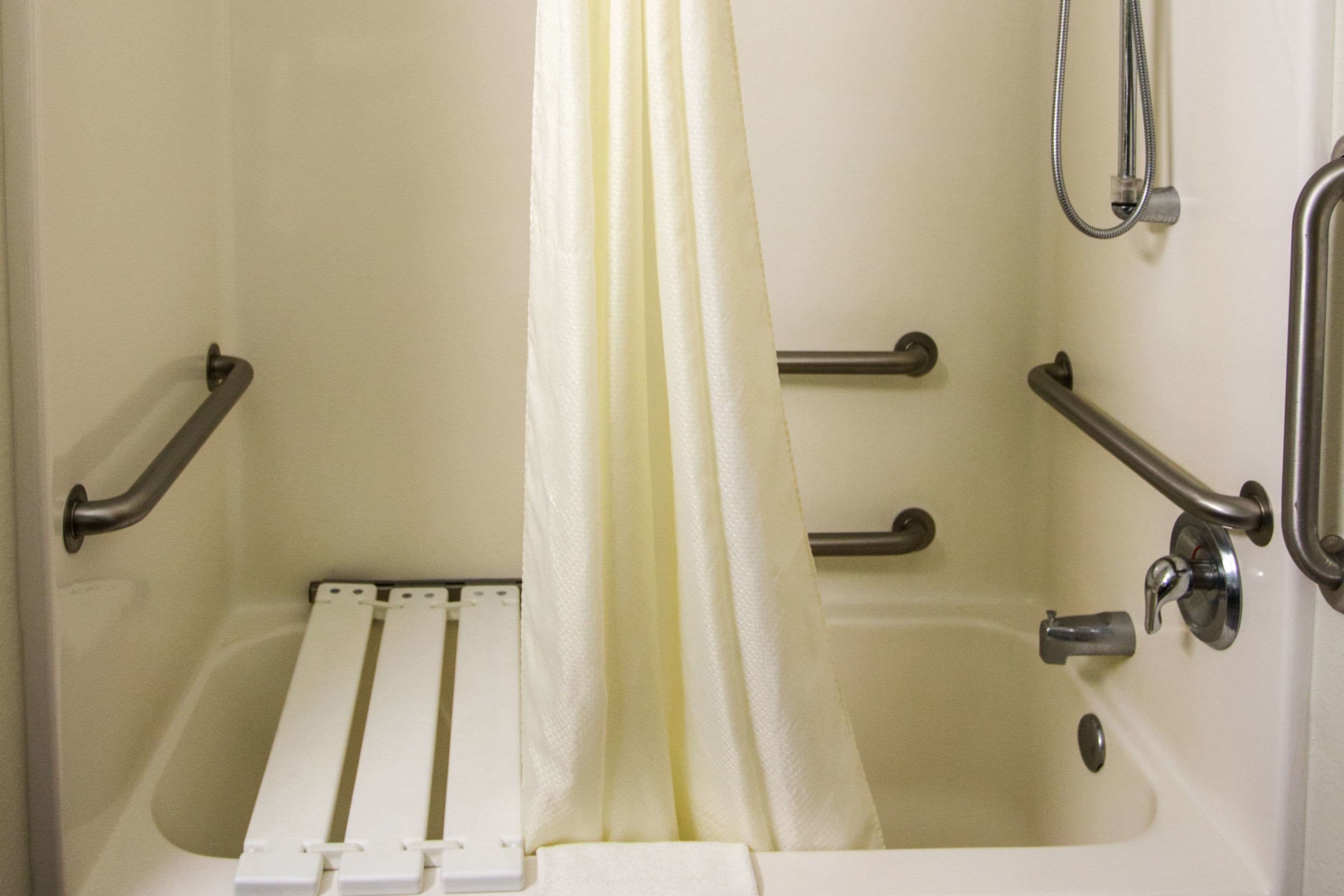 A bathtub with a showerhead, grab bars, and a white shower curtain.