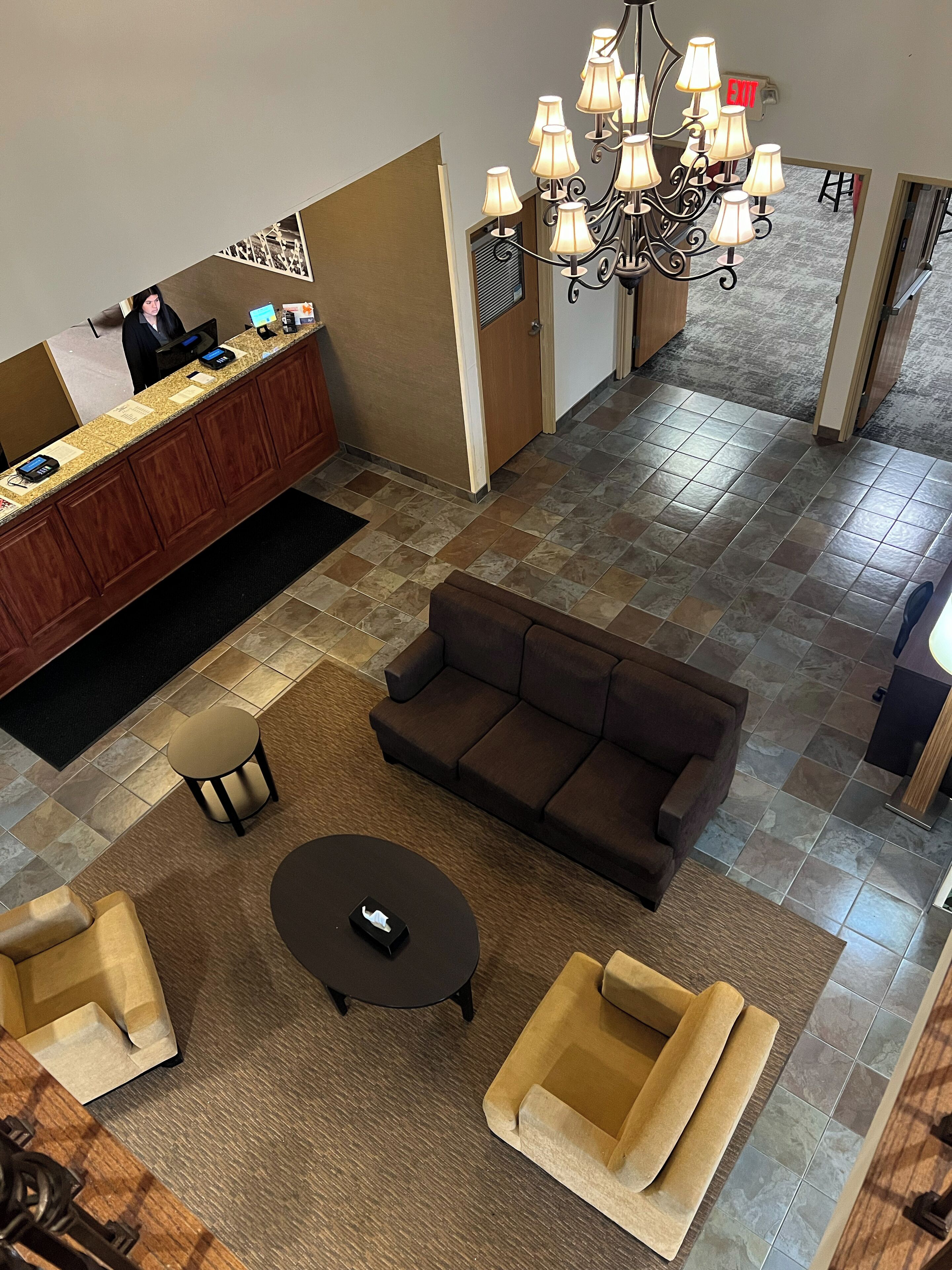 A hotel lobby with a reception desk, a brown sofa, a round coffee table, and a chandelier.