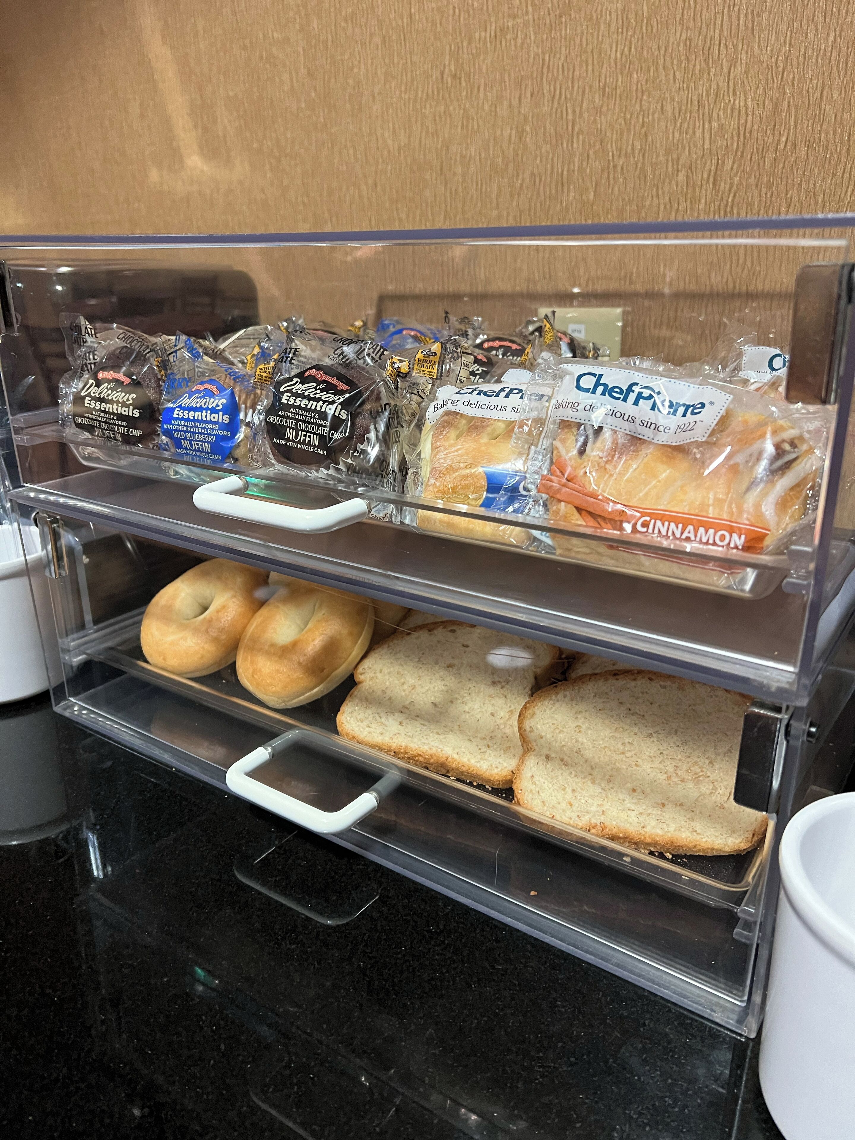 Une vitrine de boulangerie présentant divers produits de boulangerie, notamment des muffins, des bagels et du pain.