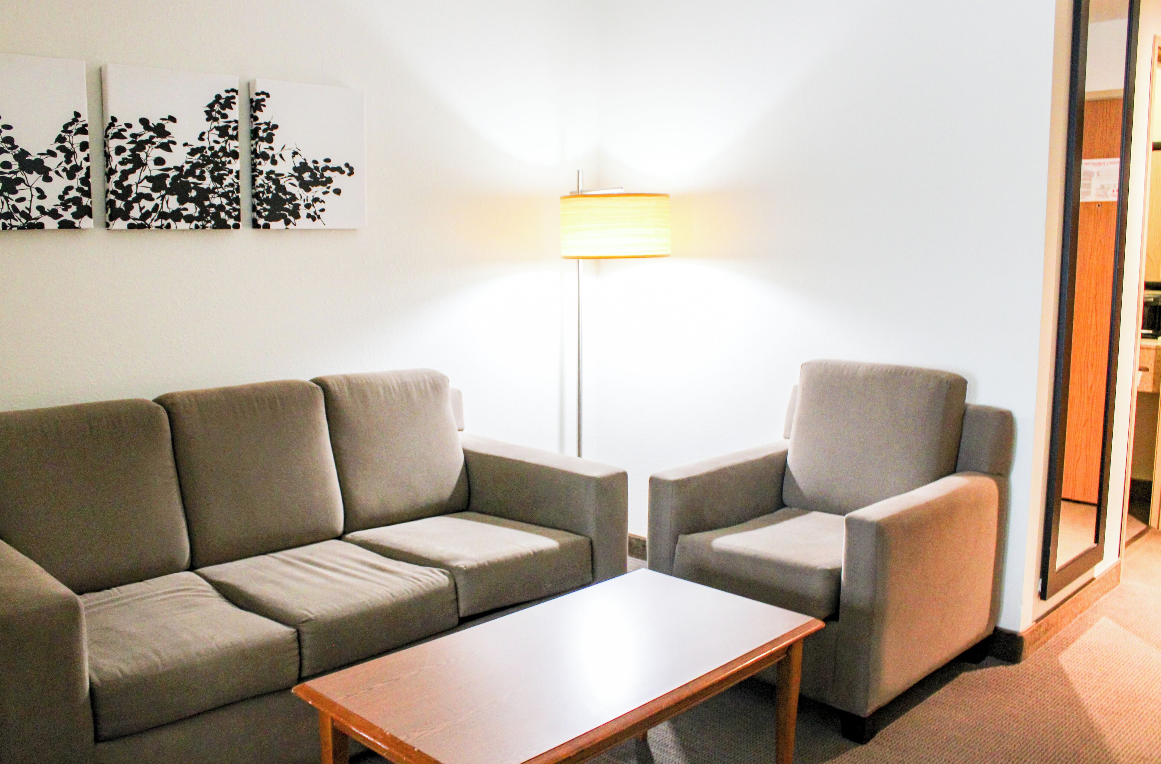 Ein modernes Wohnzimmer mit einer Couch, zwei Sesseln und einem Couchtisch. Eine Stehlampe steht zwischen den Möbeln.