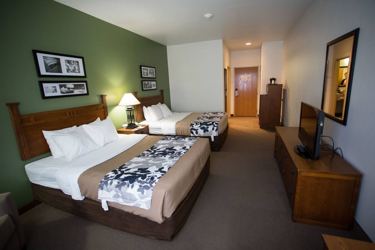 A hotel room with two beds, a desk with a computer, a mirror, and framed pictures on the wall.
