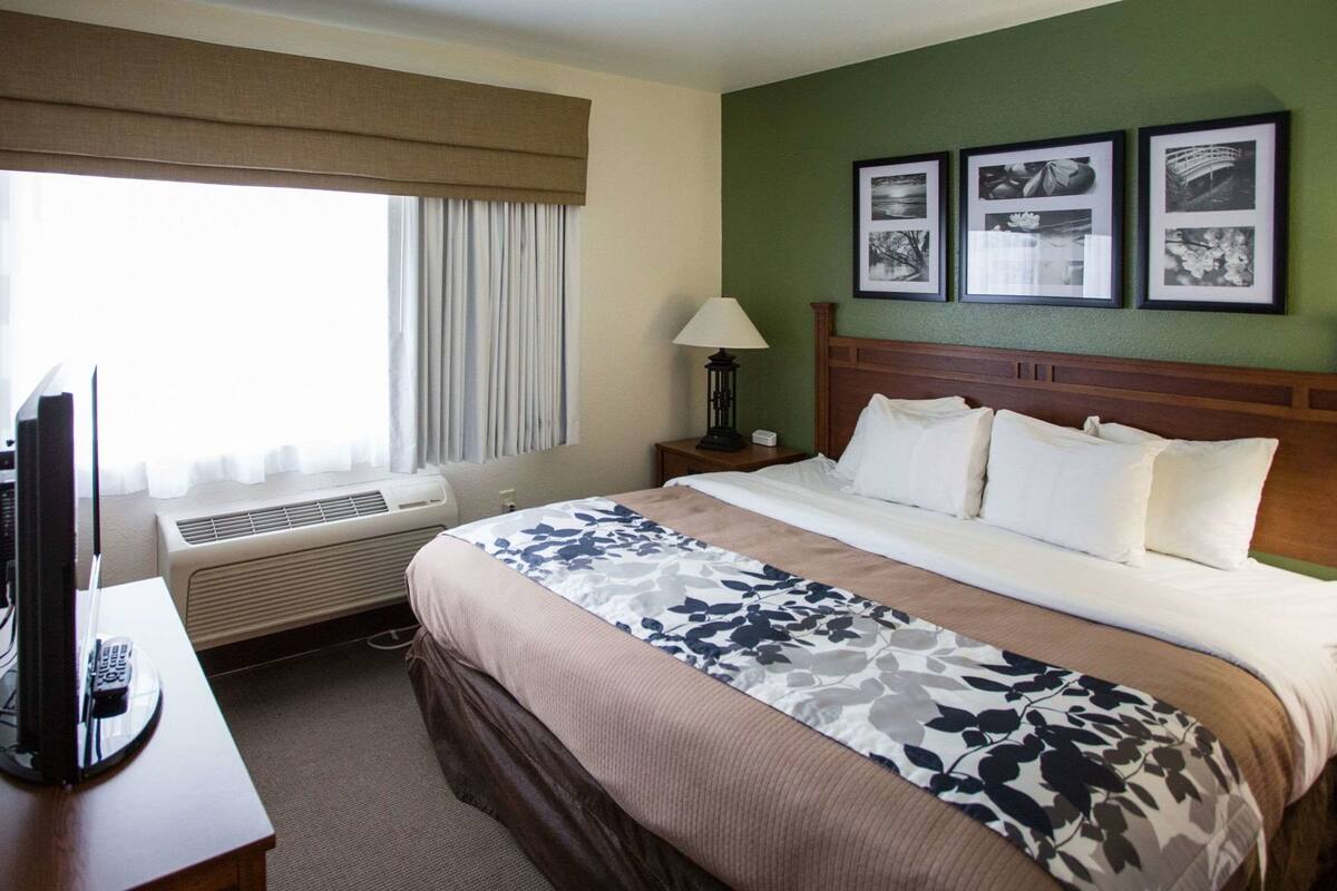 A hotel room with a bed, a desk with a computer, a lamp, and air conditioning.